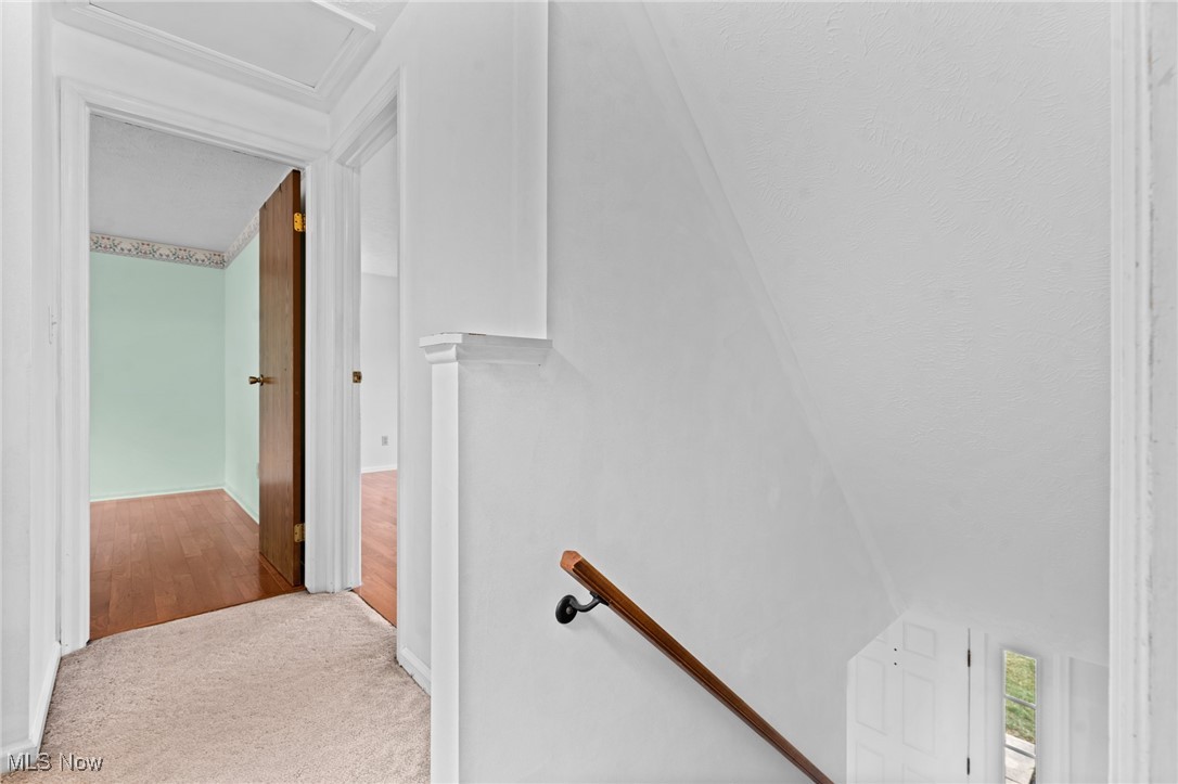 Carpeted upstairs landing beside a staircase with a wood handrail and open doorways to wood-floored rooms.