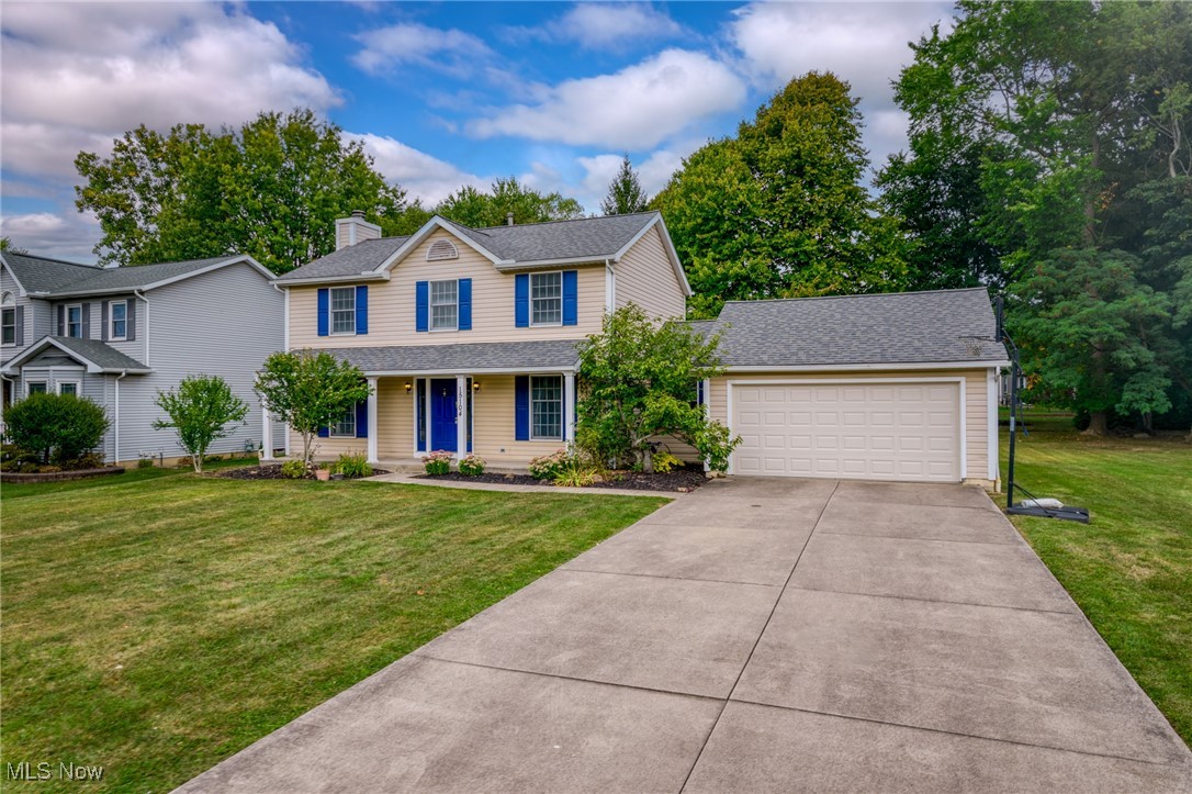 Two-story beige home with blue shutters and front door, attached garage, and broad driveway.