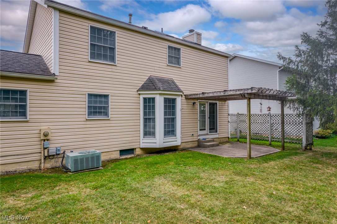 Rear of a beige two-story house with a wooden pergola shading the patio.