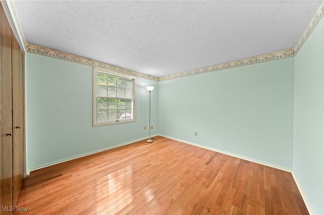 Empty bedroom with hardwood floors, pale green walls, and a floral border near the ceiling.