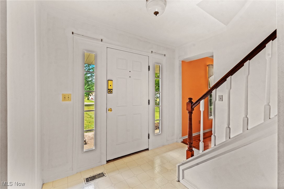 Entry foyer with a white front door, tiled floor, staircase, and orange accent wall.