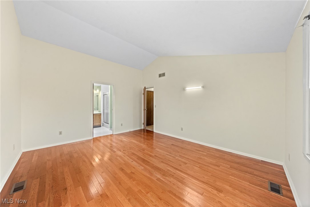 Empty room with polished hardwood floors, cream walls, and an open doorway to a bathroom.