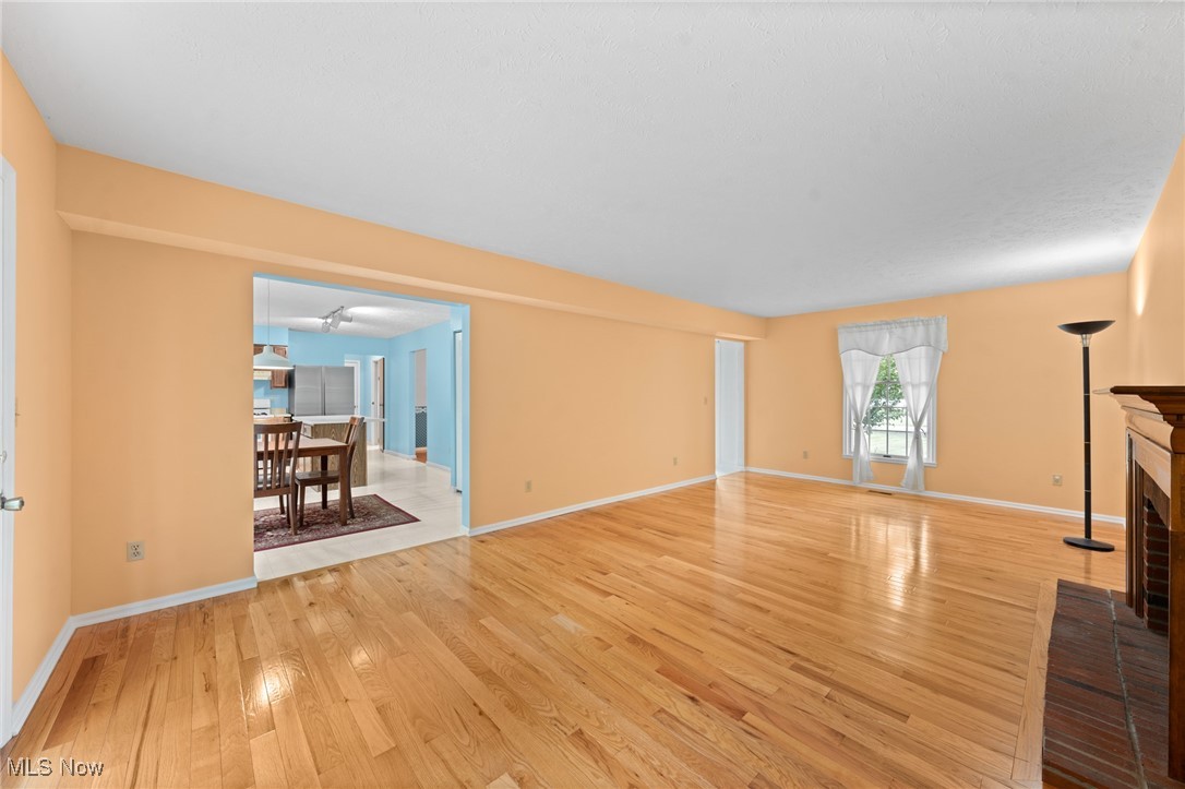 Mostly empty living room with hardwood floors, peach walls, and a brick fireplace.