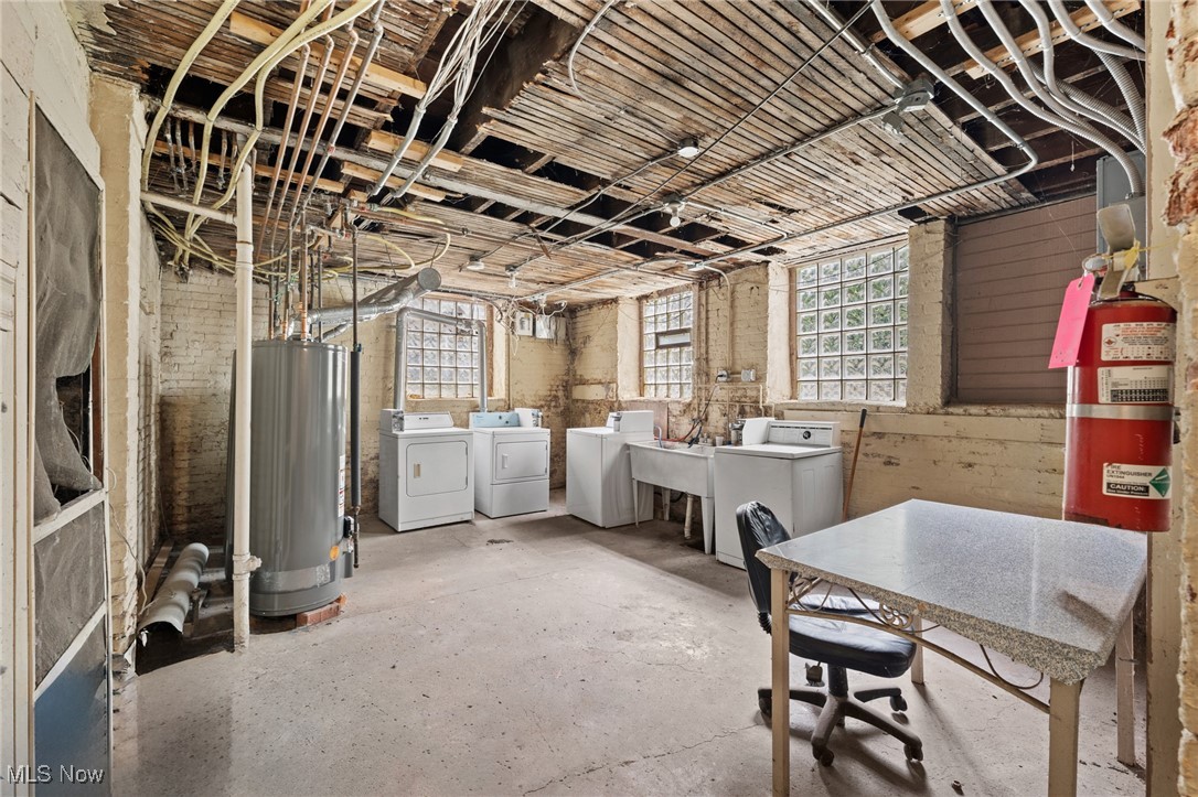 Basement laundry room with washers, utility sinks, exposed ceiling joists, and a large water heater.