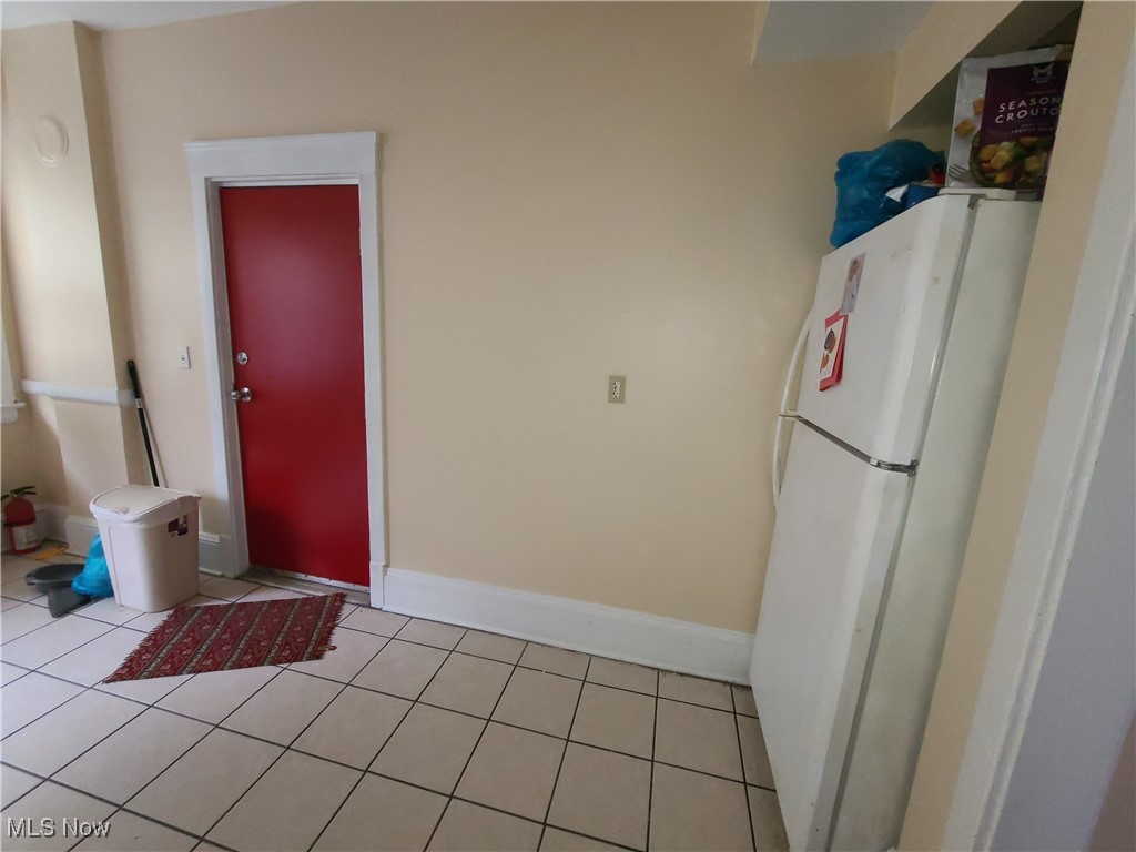 Kitchen with a white refrigerator, tiled floor, and a red door.