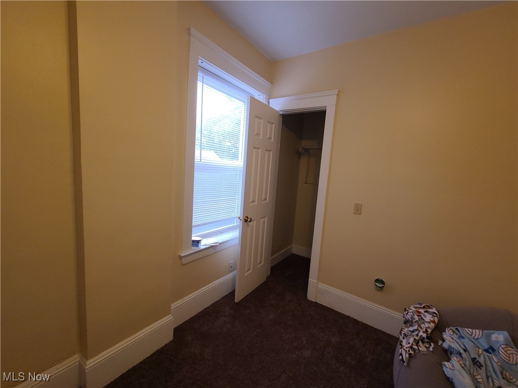 Bedroom with dark carpet, a window with blinds, and an open closet.