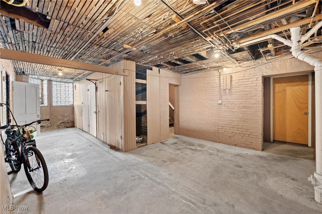 Unfinished basement with exposed joists, painted brick walls, and bicycles beside a glass-block window.
