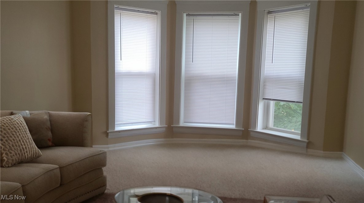 Living room with a tan sectional sofa and three tall bay windows with white blinds.
