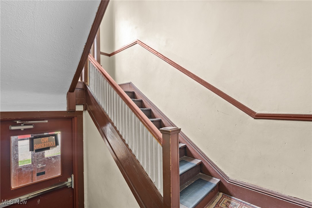Interior staircase with white balusters, dark wood rails, and a glass-paneled entry door.
