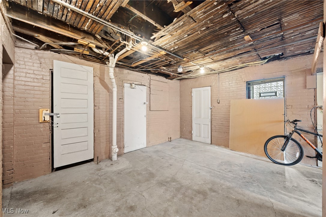 Unfinished garage with exposed ceiling joists, brick walls, concrete floor, and a bicycle.