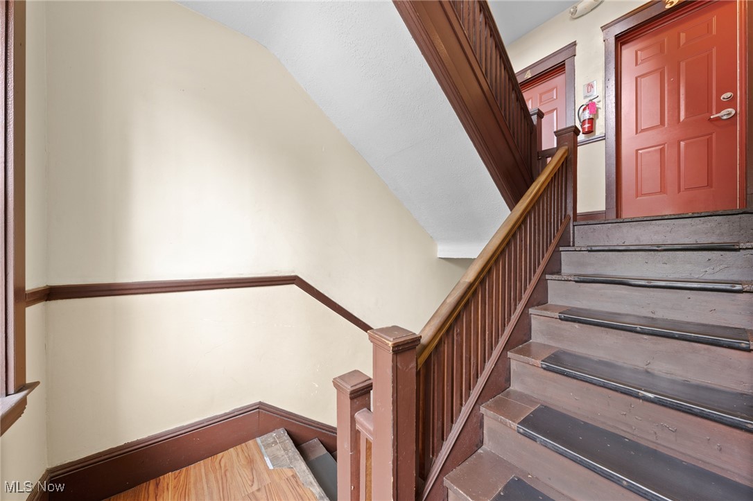 Interior stairwell with dark wood railing, worn steps, and red entry doors.