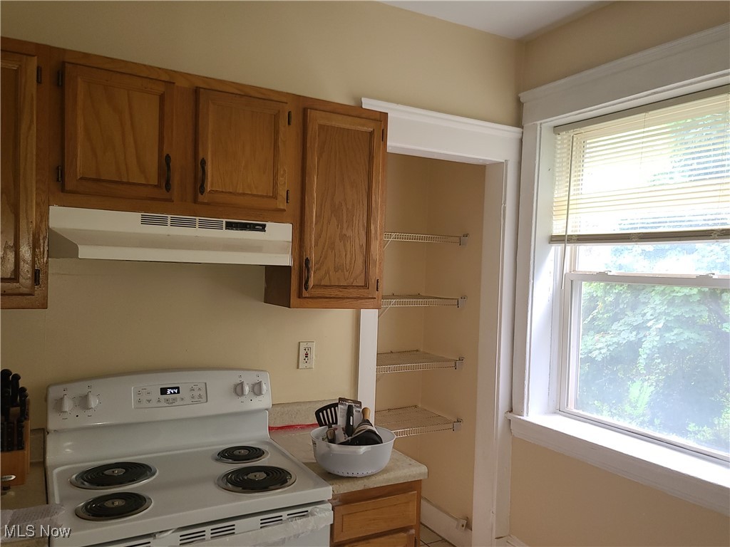 Kitchen with wood cabinets, a white electric range, open pantry shelves, and a large window.