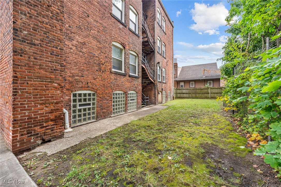 Red brick building beside a patchy fenced yard, with glass-block windows and an exterior staircase.