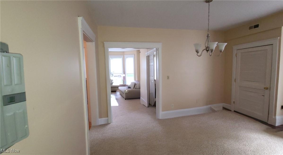Carpeted dining room with a chandelier and doorway opening to a sunlit living room.