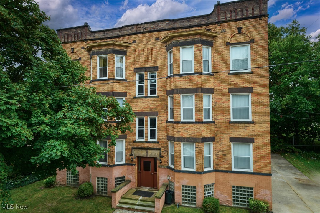 Brick residential building with projecting bay windows, a central entrance, and mature trees.