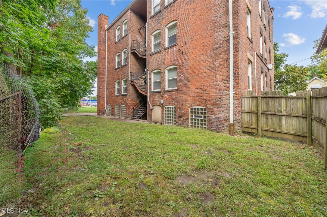 Red-brick building with metal fire escapes beside a grassy, fenced yard.