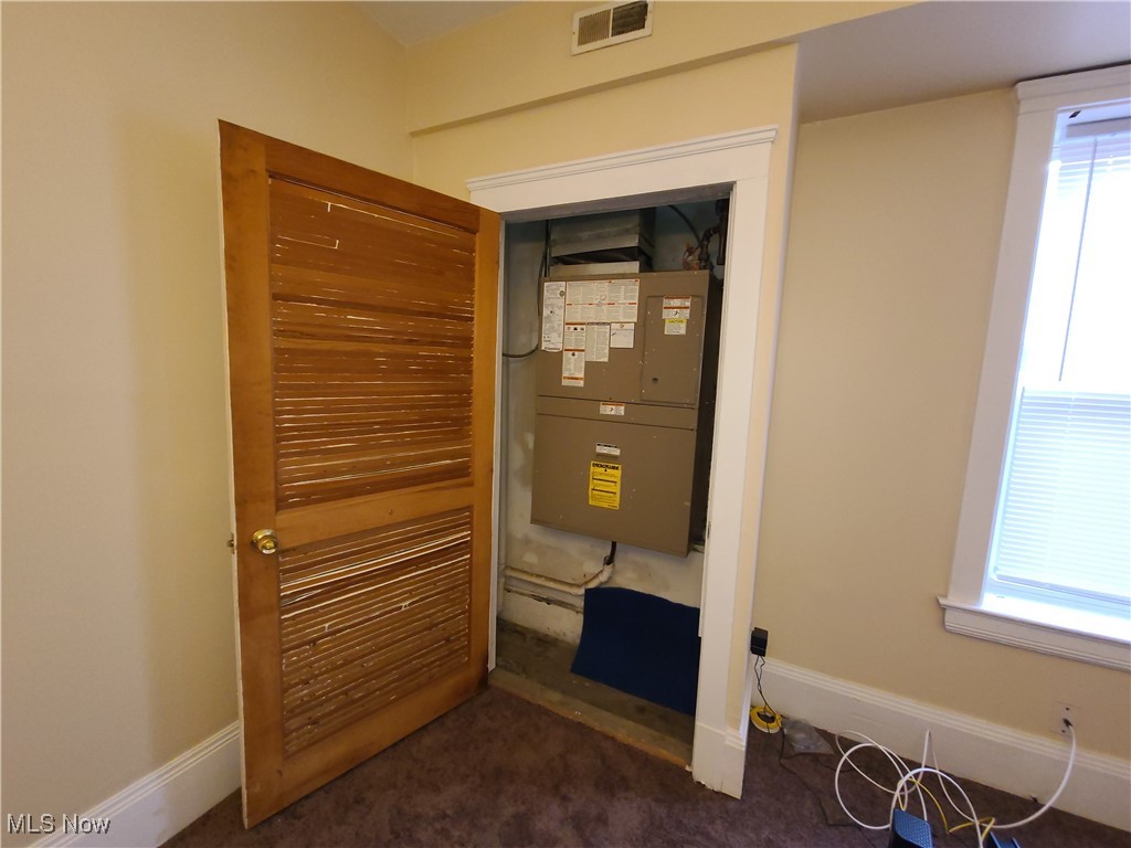 Utility room with a wall-mounted HVAC unit behind an open wooden louvered door.