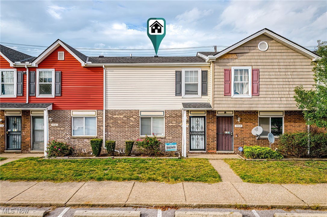 Cream-and-brick townhouse between red and tan homes, with a small front lawn and sidewalk.