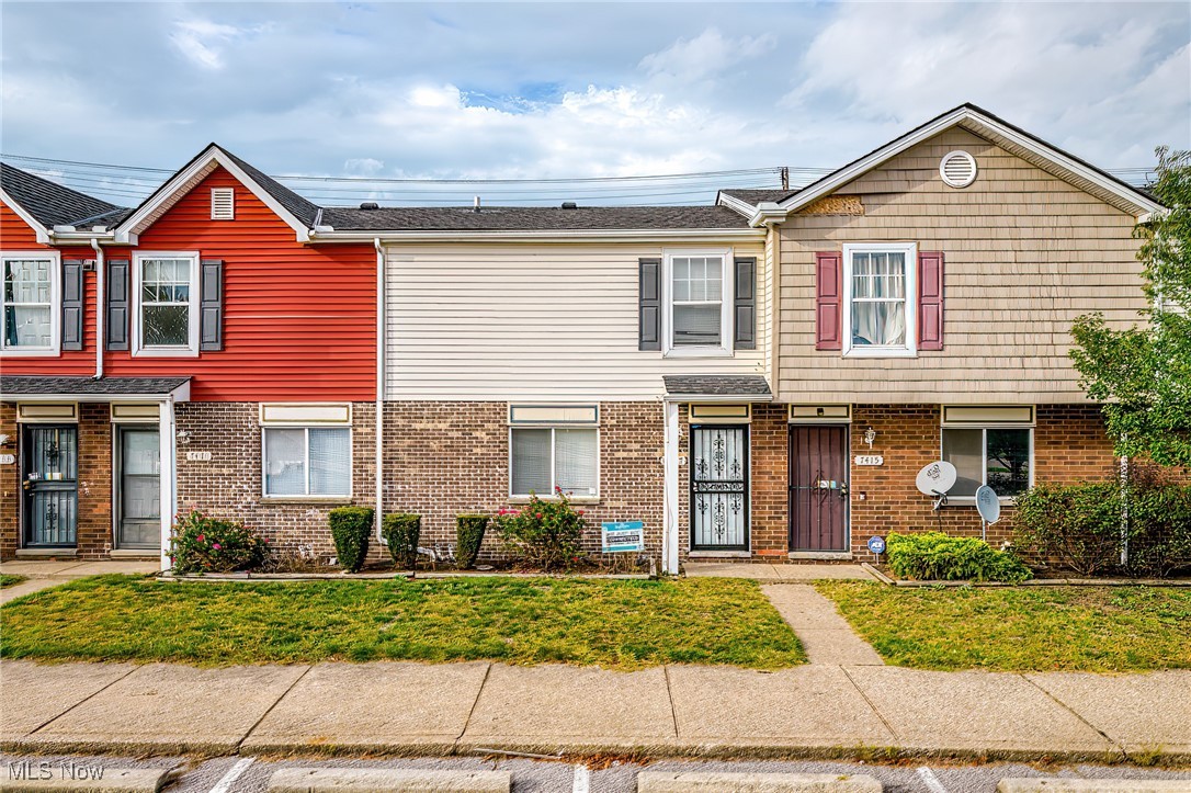 Attached townhouses with brick lower levels, red and tan facades, and small front lawns.