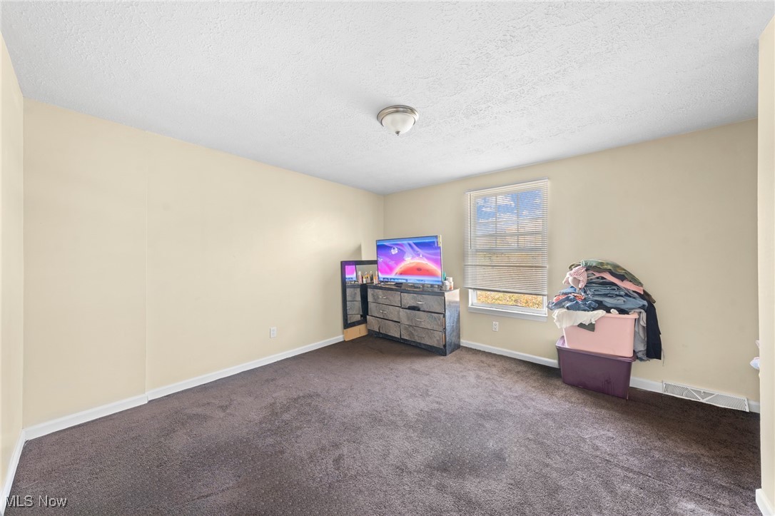 Bedroom with a dresser and television beside a window, and clothing piled on storage bins.