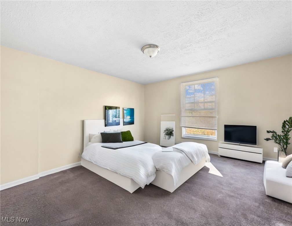 Staged bedroom with a white bed, gray carpet, and a window with blinds.