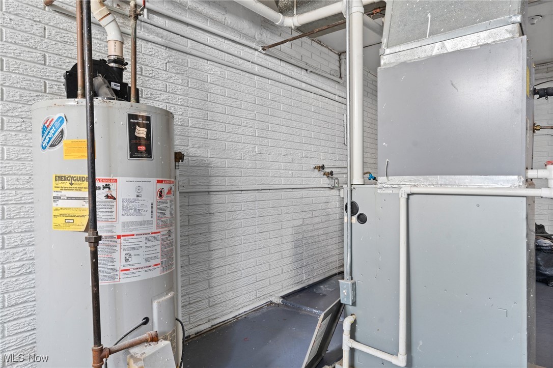 Mechanical room with a tank water heater beside a large furnace and exposed ductwork.
