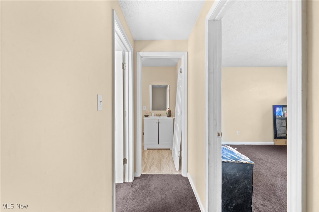 Carpeted hallway leading to a bathroom, with an open bedroom doorway on the right.
