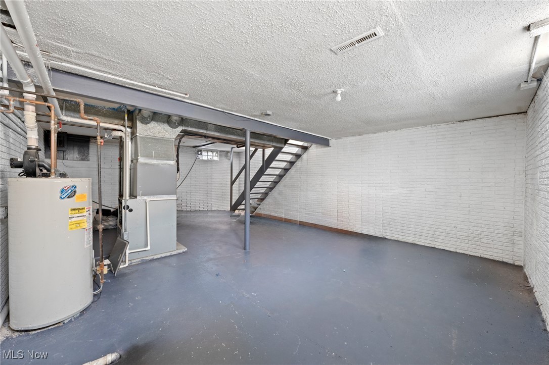Unfinished basement utility room with a water heater, furnace, exposed pipes, and stairs.