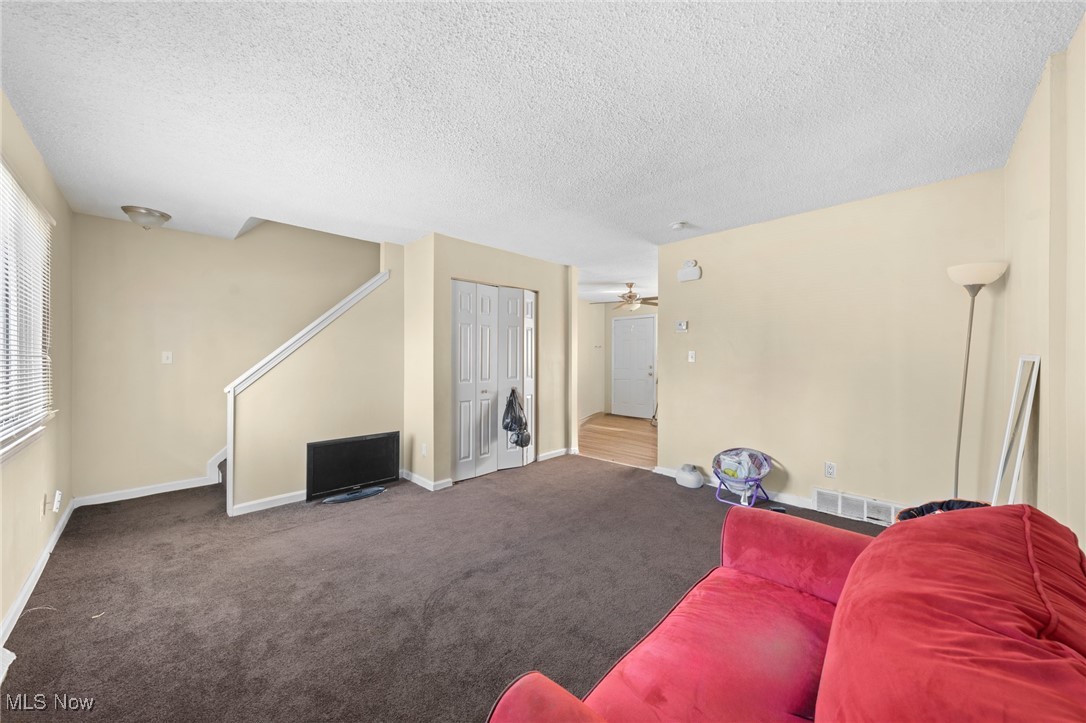 Living room with dark carpet, red sofa, television, and stairs.