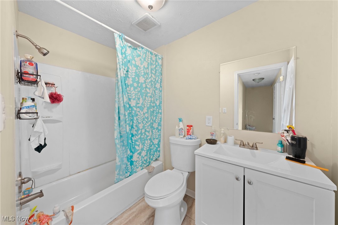 Bathroom with a turquoise floral shower curtain, white tub, toilet, and vanity.