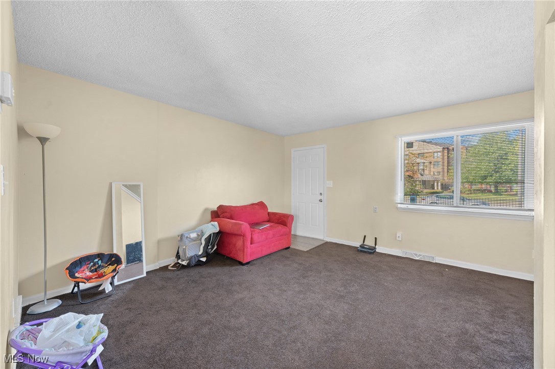 Living room with a red loveseat, brown carpet, and a large window with blinds.