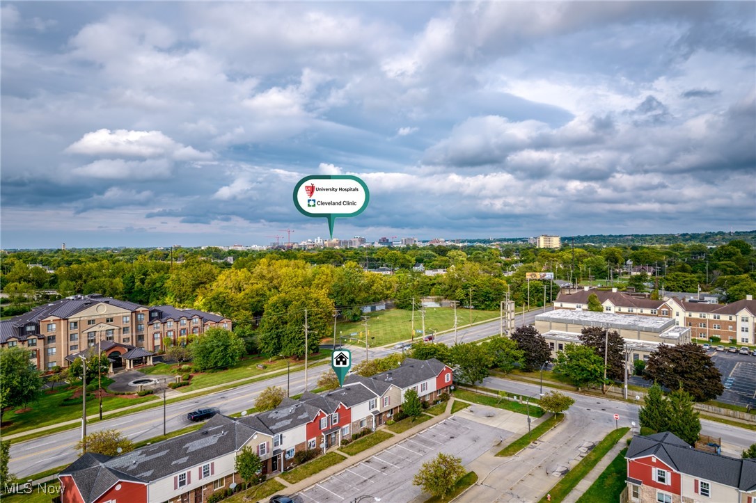 Aerial view of townhomes beside a road, with trees and a distant skyline beneath cloudy skies.