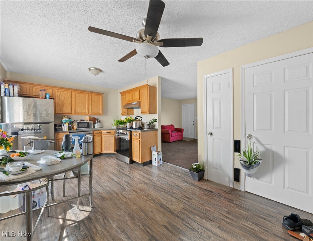 Kitchen with honey-colored cabinets and stainless steel appliances, opening to a living area with a red sofa.