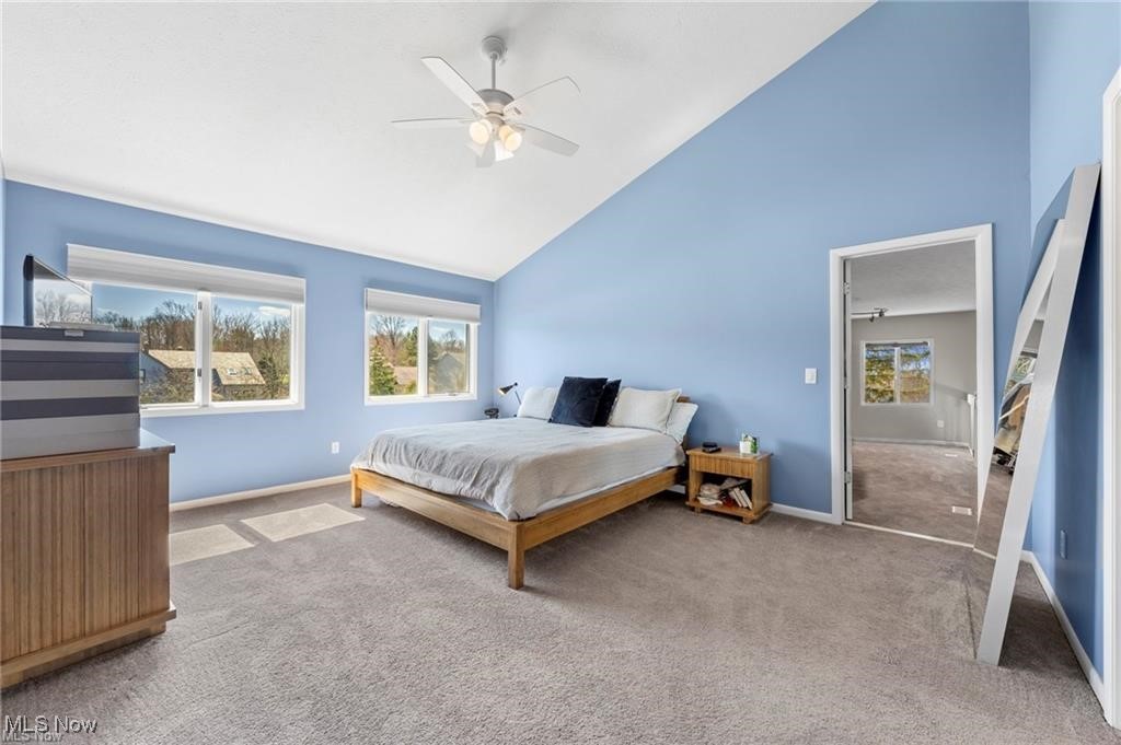Blue bedroom with a wooden bed, high sloped ceiling, ceiling fan, and windows.