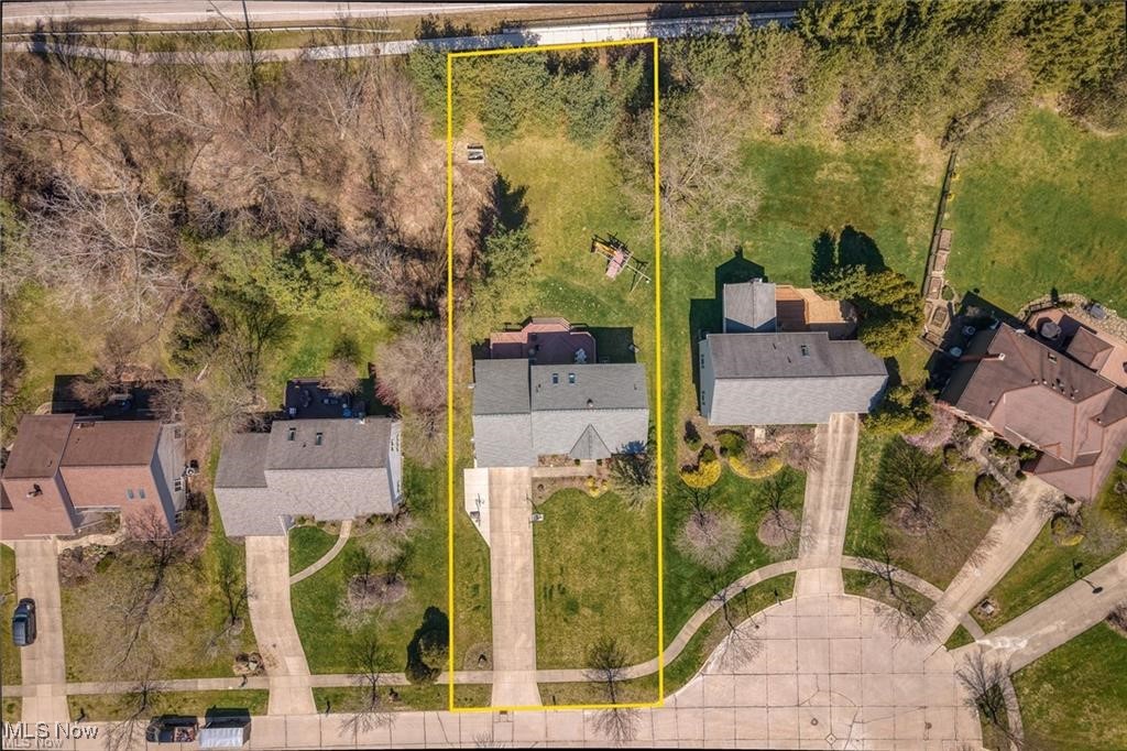 Aerial view of a house and its lot outlined in yellow, with a large backyard.