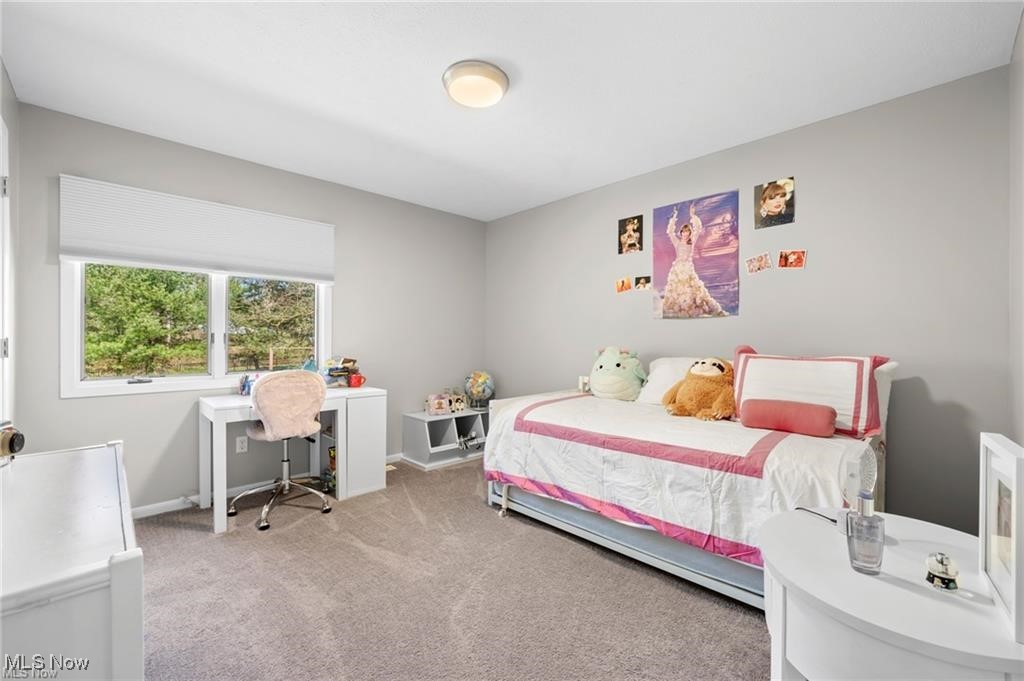 Bedroom with a white-and-pink bed, desk, and window overlooking trees.