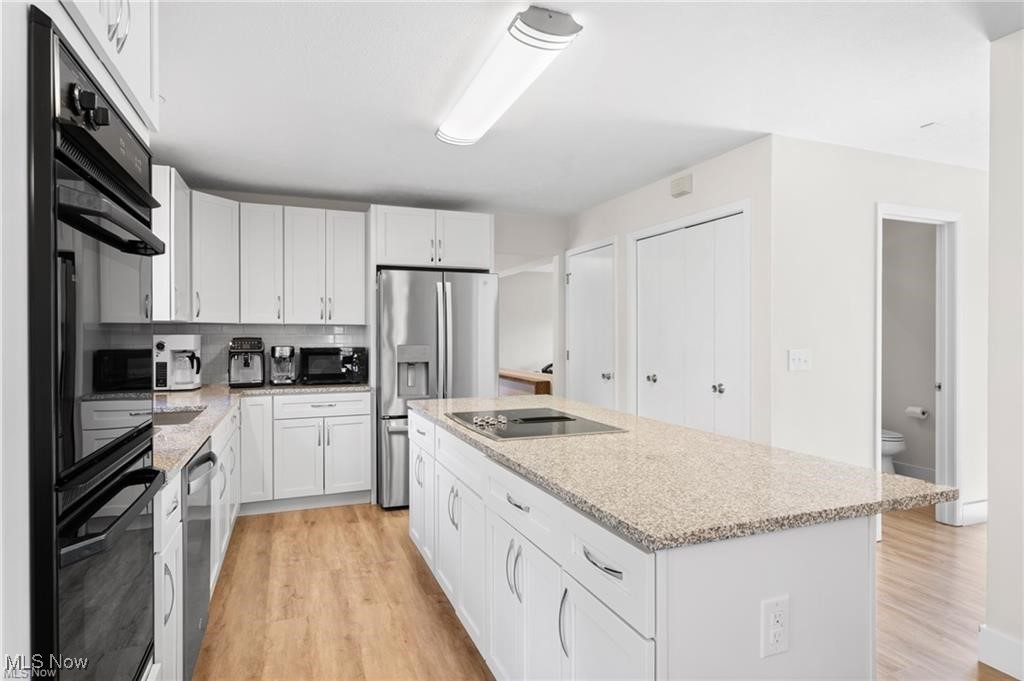 White kitchen with stainless steel appliances and a large granite island with cooktop.