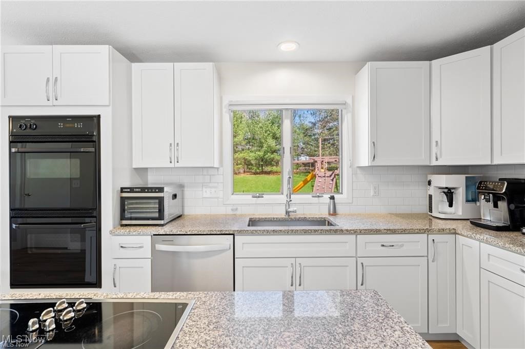 Bright white kitchen with granite counters, double wall oven, island cooktop, and a backyard playset visible through the window.