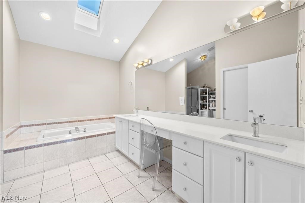 Bathroom with a tiled soaking tub, double-sink vanity, wall-length mirror, and skylight.