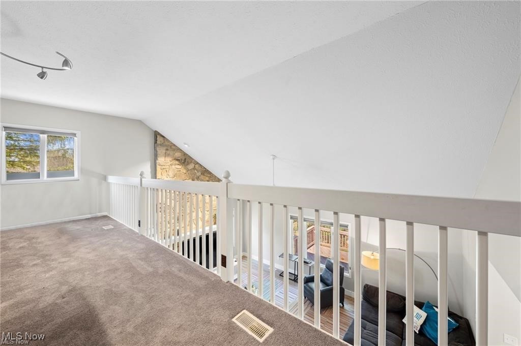 Carpeted loft overlooks a living room, with white railings and a tall stone fireplace.