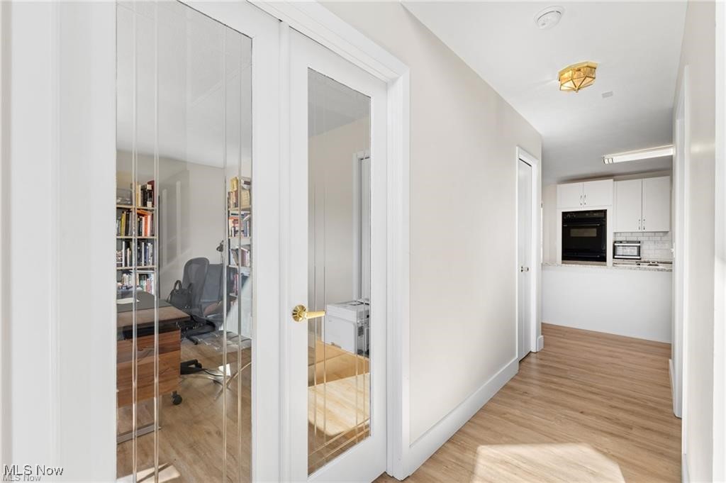 Hallway with glass-paneled office doors, light wood-look flooring, and a kitchenette at the far end.