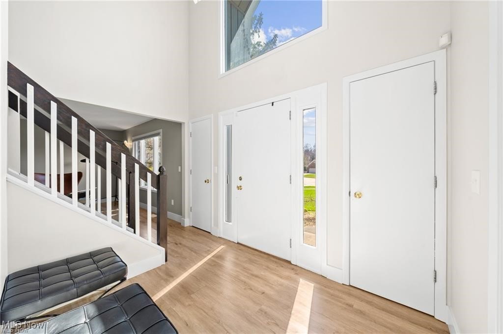 Two-story entry foyer with a white front door, tall windows, wood flooring, and a dark-and-white staircase.