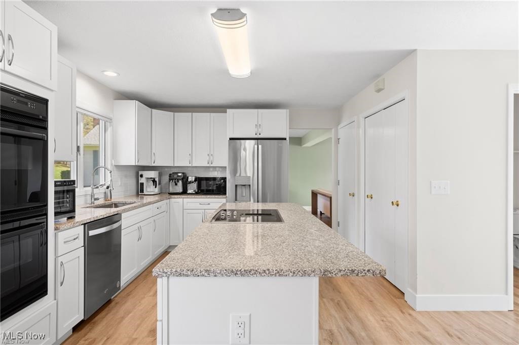 Kitchen with white cabinetry, stainless steel appliances, and a large granite island with a cooktop.