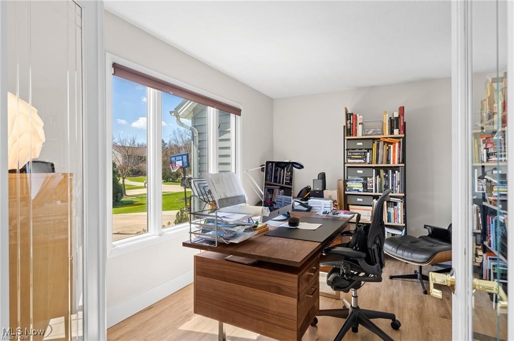 Home office with a large wooden desk, bookshelves, and wide windows overlooking the lawn.