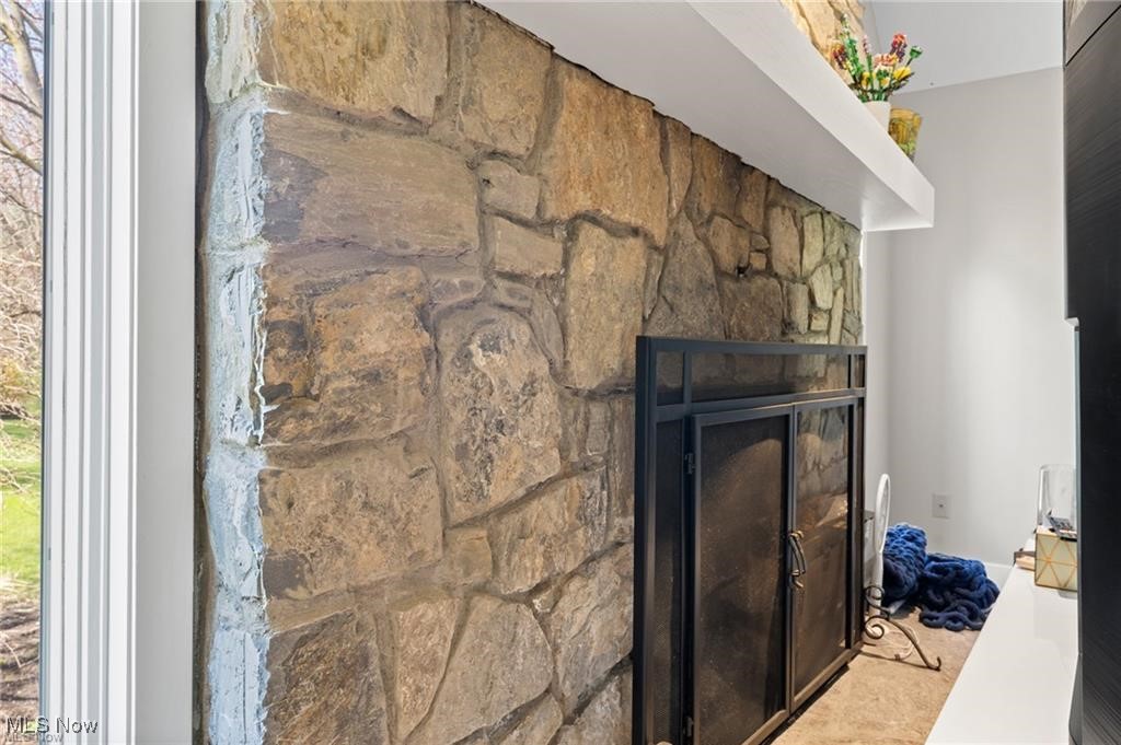 Stone living room fireplace with a black metal insert and tall window beside it.