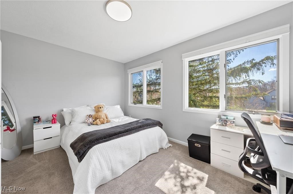 Bedroom with a white bed, teddy bears, and large windows overlooking trees.