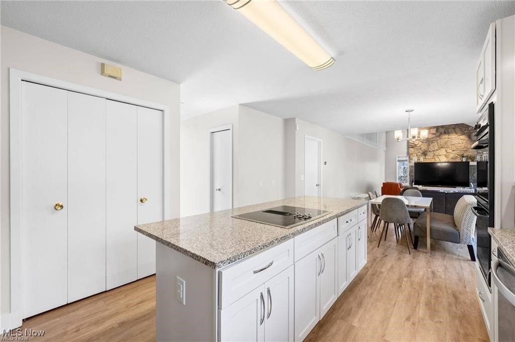 Kitchen with a granite island and cooktop, opening to a dining area and stone fireplace.