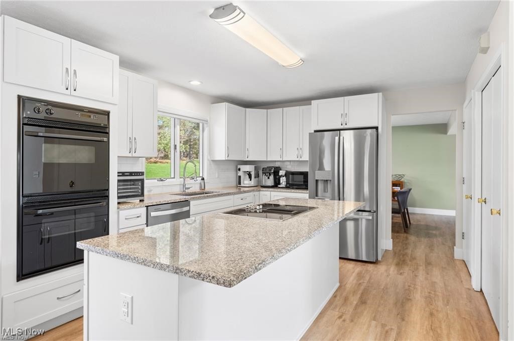 Bright white kitchen with a granite island, stainless steel appliances, and a window overlooking the yard.