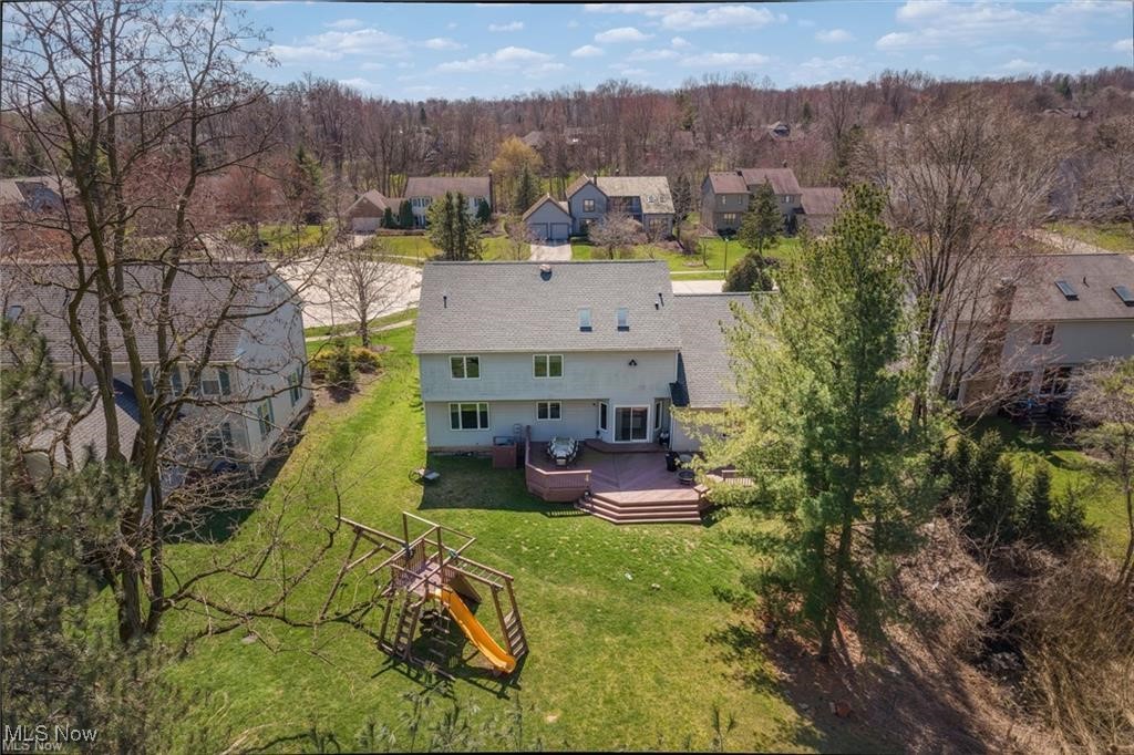 Aerial view of a two-story home with a raised deck, backyard playset, and wooded surroundings.
