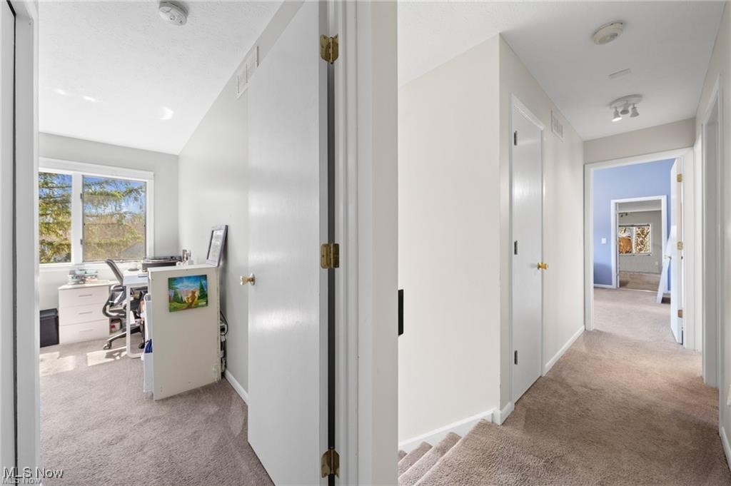 Carpeted upstairs hallway with an open home office and a blue room visible at the far end.